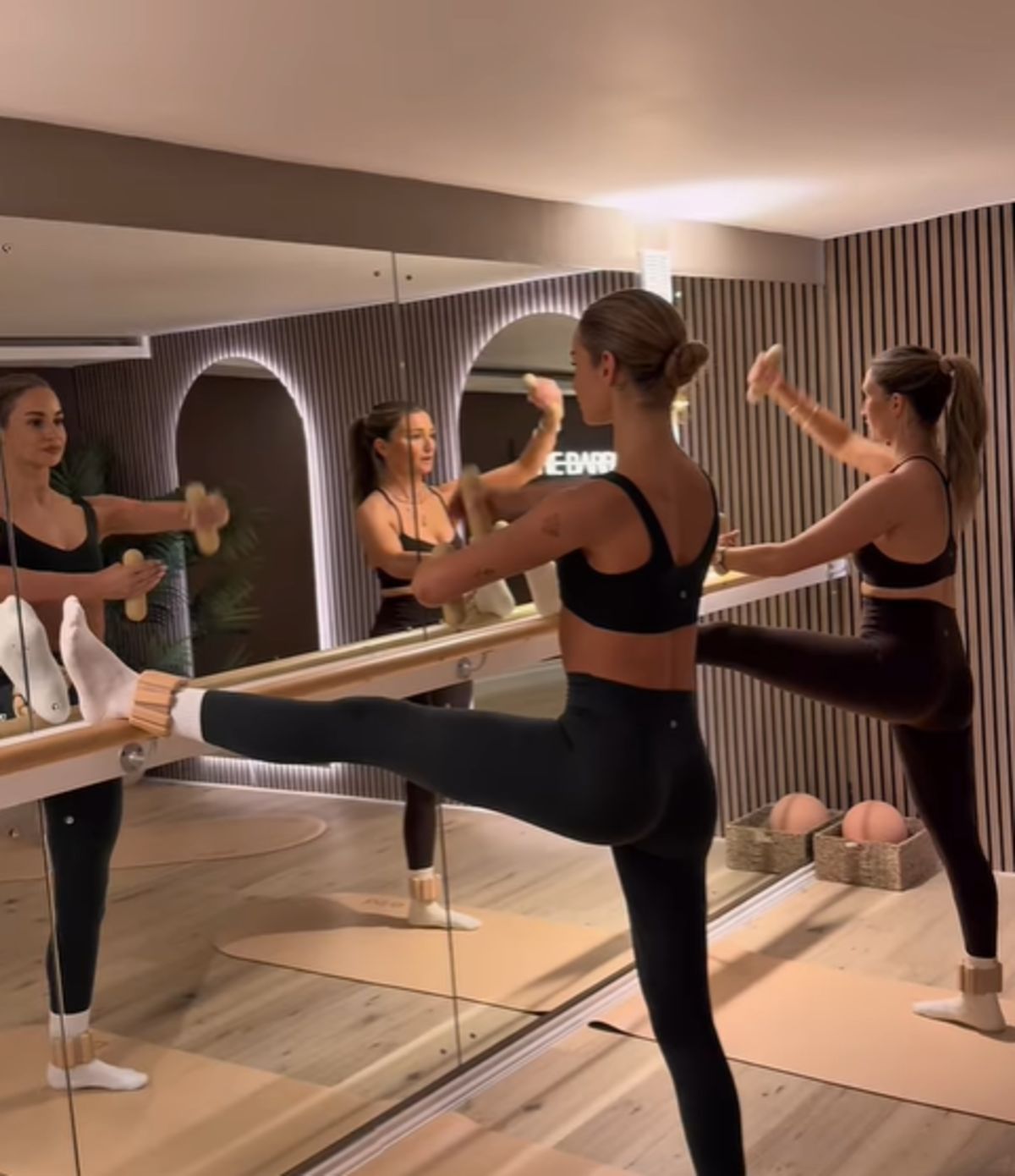 Barre class in progress at the studio, mirrored wall and warm wooden barre